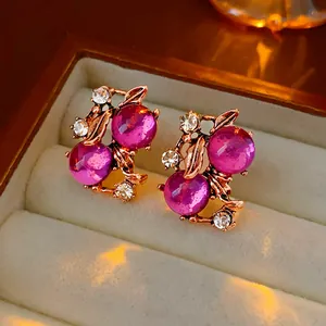 Close-up of vintage magenta berry stud earrings in a warm beige jewelry box