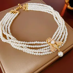 Detail of vintage court style multi-strand pearl necklace with a gold bee pendant.