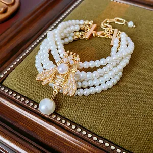 Close-up view of a multi-strand vintage pearl bracelet with golden bee charm detail.