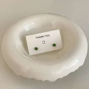 Detail view of mini green stud earrings on a white thank you card in a ceramic dish.