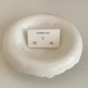 Close-up of minimalist pink candy bean stud earrings on a white "Thank You" display card.