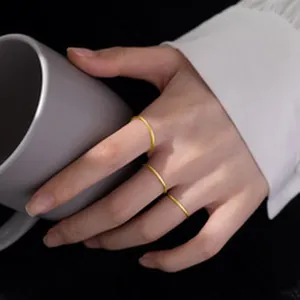 Detailed view of three minimalist gold-plated silver rings worn on a hand holding a cup