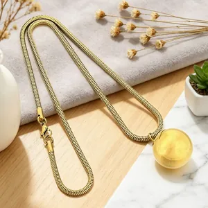 Detail of golden snake chain necklace featuring a large smooth spherical ball pendant