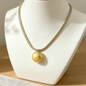 Detailed close-up of a bold gold-toned snake chain necklace featuring a large ball pendant.