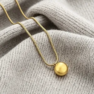 High-quality close-up of a gold snake chain necklace featuring a polished ball pendant on grey knit