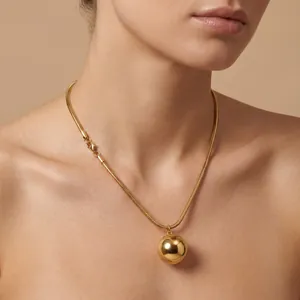Detailed view of a large gold ball pendant on a snake chain necklace worn by a model