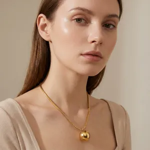 Elegant woman wearing a gold snake chain necklace with a large round ball pendant