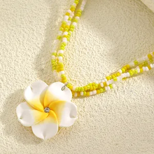 Macro view of white and yellow frangipani flower pendant on a beaded necklace