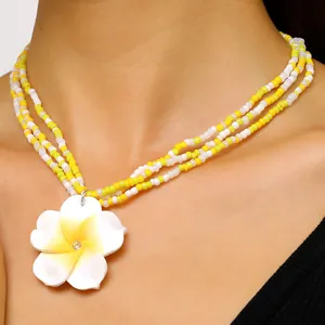 Close-up of yellow and white beaded necklace with frangipani flower pendant detail.