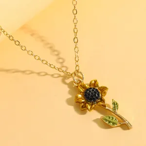 Gros plan détaillé d'un pendentif tournesol doré avec centre noir et feuilles vertes.