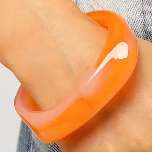 Nahaufnahme eines orangefarbenen marmorierten Harzarmreifs mit geometrischem Design
