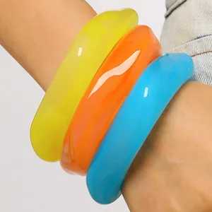 Nahaufnahme von drei klobigen marmorierten Harzarmreifen in Gelb, Orange und Blau am Handgelenk.