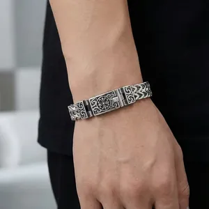 Primo piano di un bracciale da uomo in acciaio al titanio con intricati motivi a ricciolo.