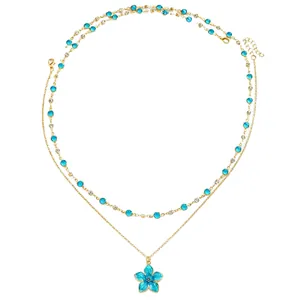 Close-up of layered gold necklace with blue enamel flower and crystal beads.