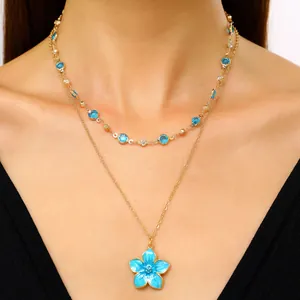 Close-up view of a layered gold necklace set featuring a vibrant blue enamel flower pendant.