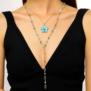 Detail shot of a layered gold necklace featuring a blue enamel flower and crystal accents