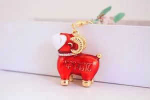 Détail d'un porte-clés bélier rouge mignon avec collier en strass et cornes dorées.