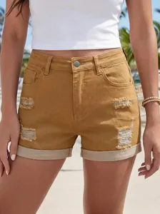 Dettaglio degli shorts di jeans a vita alta color senape con strappi e orli risvoltati.