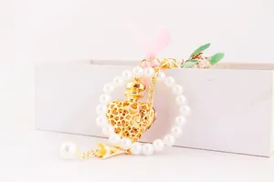 Detailed view of a cute gold perfume bottle keychain with pink ribbon and white pearls