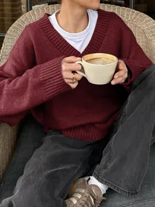Woman wearing a cozy burgundy V-neck knitted sweater while holding a cup of coffee