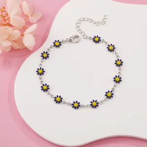 Detailed shot of a silver chain bracelet featuring blue daisy charms on white board