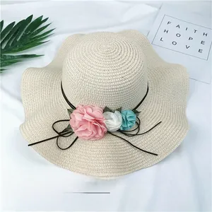Close-up detail of beige straw sun hat featuring three colorful fabric flowers and tie