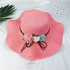 Detail view of pink woven straw sun hat with colorful decorative flowers and wave brim