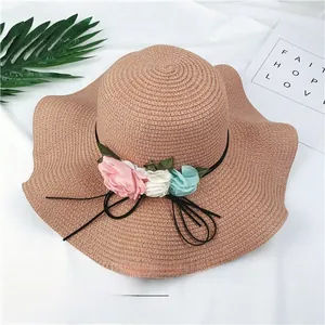 Detailed view of women's stylish wide-brimmed straw sun hat with decorative fabric flowers