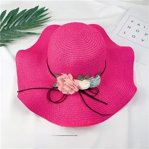 Elegant hot pink straw sun hat featuring fabric flowers and a wavy brim for summer