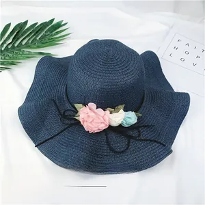 Detail view of a navy straw hat with decorative flowers and wide brim.