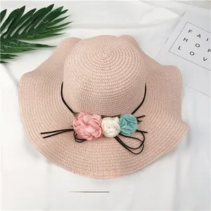 Detailed view of pink straw sun hat featuring fabric flowers and a wavy brim design