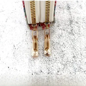 Detailed macro view of dual light gold metal zippers on a luxury card holder wallet