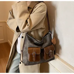Detailed view of washed denim shoulder bag featuring dual brown leather flap pockets.