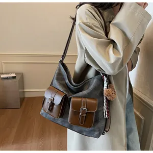 Large grey denim texture shoulder bag with brown leather pockets carried by model