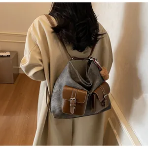 Fashionable gray denim canvas hobo bag with two brown buckled pockets shown on model