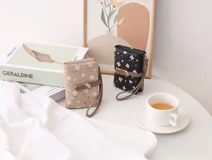 Detail of two chic floral print short wallets with wrist strap in lifestyle setting