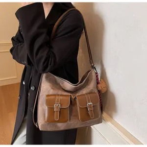 Large brown hobo shoulder bag with dual buckle pockets worn with a black coat