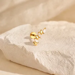 Close-up of a gold-plated silver cartilage piercing with marquise-cut crystals on white rock