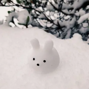 Close-up of a white rabbit squishy toy sitting in a beautiful winter snowy landscape