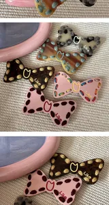 Detailed view of stylish bow hair clips featuring Like embroidery and stitched edges.