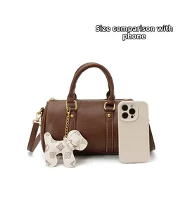 Brown Boston pillow bag shown with a smartphone for size comparison.