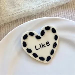 Detail of a heart-shaped hair clip with black wool edge and Like text.