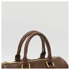 High-quality close-up detail of brown Boston bag handles with neat white stitching and gold hardware