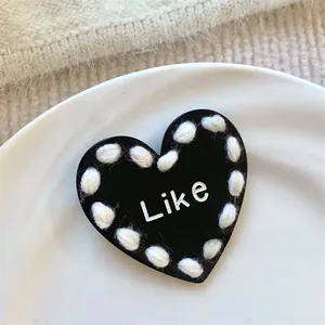 Detailed macro view of black heart shaped hair clip with white yarn edge and Like text