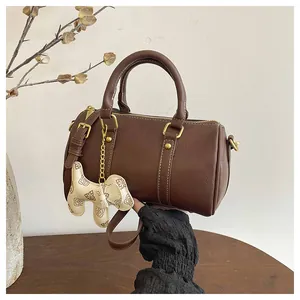 Detail view of brown Boston pillow bag held by hand, showcasing dog charm and texture