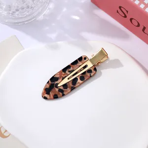 Detail of a leopard print acetate hair clip with golden metal duckbill base on white plate.
