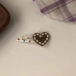 Detail of a white heart-shaped BB hair clip with colorful dots and "LOVE" text.