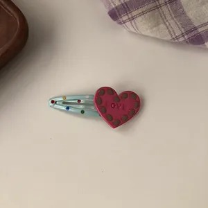 Close-up detail of a sweet pink heart hair clip with embossed LOVE text and dots