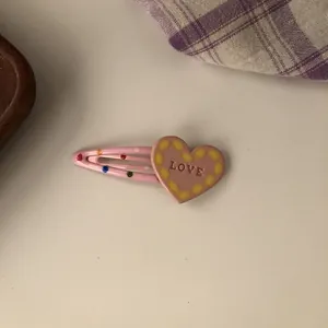Close-up of pink heart hair clip with yellow dots and LOVE engraving in detail