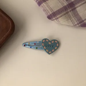Close-up of cute blue heart hair clip with colorful dots and LOVE text decoration